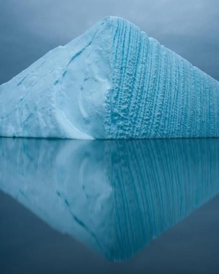 Eroding blueish iceberg reflecting in the water, a perfect triangle.