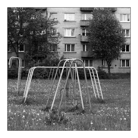 Verfallene Spielgeräte auf einer Wiese. Dahinter Plattenbauten aus Sowjetzeiten. Wir befinden uns in Rezekne, Letgalen, Lettland.