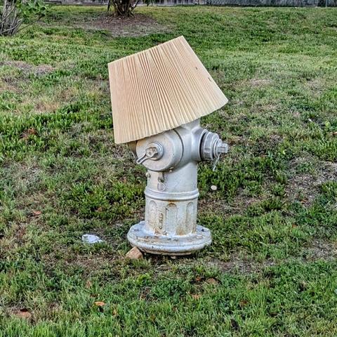 A silver painted traditional US fire hydrant wearing a pleated lampshade at a jaunty angle