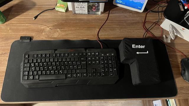 Schreibtisch mit XXL Mousepad. Darauf eine schwarze Tastatur und rechts daneben eine XXXXL Entertaste. (Voll funktionsfähig)