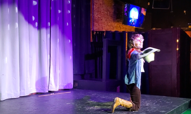 Austin Tacious, still dressed as a cowboy, kneeling on stage and holding his cowboy hat out dramatically.