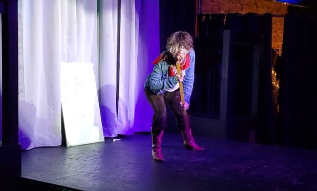Austin Tacious, still dressed as a cowboy, singing intensely into the end of a meter stick like it's a microphone
