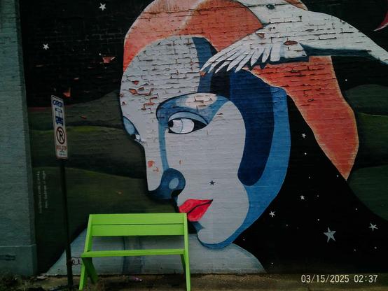 Colorful mural of a woman's face with a bird, and a lime green handmade bench sitting at a bus stop.