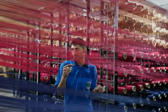 An worker checks a loom with red threads in a carpet factory.