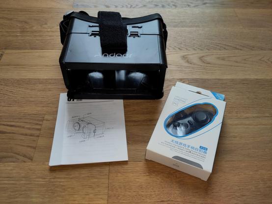 Foto der im Post genannten Smartphone-VR-Brille inkl. Anleitung und des originalverpackten Gamepads.