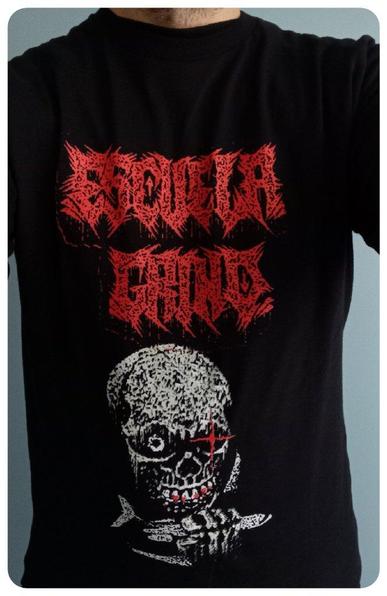 T-shirt du groupe Escuela Grind pour le concert au Sylak 2024. 
Encore un épisode de "Le groupe est bon en concert mais le t-shirt est moche"... 
Le nom du groupe en rouge est à la limite du lisible. 
Un crâne (moche) qui tient un avion dans sa main engrais
en-dessous. 
Dans le dos, on retrouve les dates de la tournée européenne ainsi que des instructions que l'on peut trouver dans les avions A-330 ou A-800.