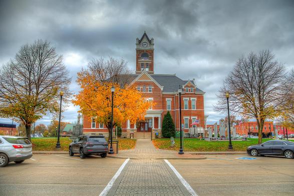 A historic brick building stands prominently, featuring a clock tower and surrounded by vibrant autumn trees.