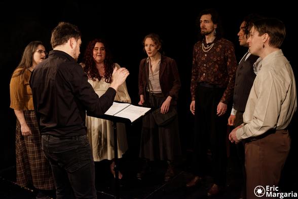 Sur la scène, le chef de choeur dirige les six chanteurs et chanteuses en arc de cercle