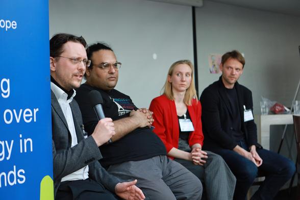 A man on a panel with three other persons holding a microphone and talking to an audience.