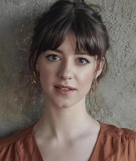 Daisy Edgar-Jones in a light brown dress with v-neckline. Her long brown hair in an up-do with bangs and brown eyes.