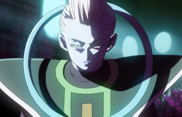 an image from the movie, a slender white-skinned  figure  with white hair and large triangular shoulder pads is looking at the viewer, light coming into the shadowy interior behind him 