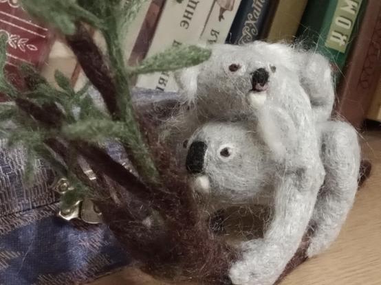 There is a craft on the bookshelf. This is miniature interior toy, made from nettle fibers by dry felting, in the form of a koala with a baby. An adult koala sits on a eucalyptus branch and holds a branch with one paw and eats leaves. The baby clings to the mother koala's back with all paws, its head is turned to the side.
Thank you for your attention!