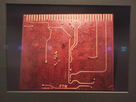 a red PCB board with few connections, exhibited in a frame
