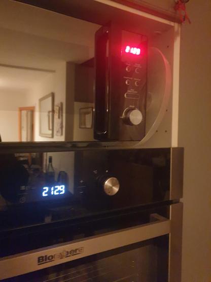 A black microwave with a very red LED display.