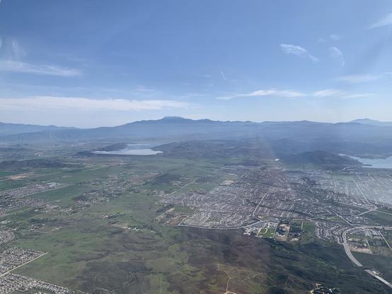 Aerial view on a sunny, but hazy, day over suburbs, fields, reservoirs, foothills, and mountains