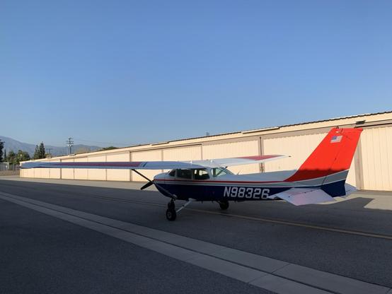 A light airplane (it’s a Cessna 172) stands on the pavement beside  row of hangars