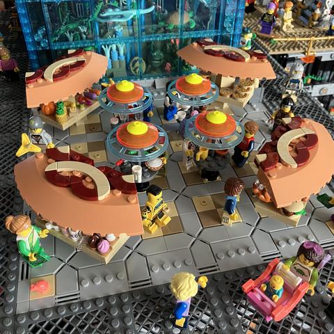 Overview of the plaza with four different food stalls and four stand up tables. 