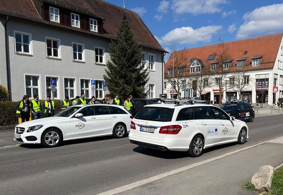 Die automatisierten Versuchsfahrzeuge der Uni Ulm (weiß, im Vordergrund) und von Bosch (blau, im Hintergrund) bei der Demofahrt zum kooperativen Fahren. Dafür wurde an der Pilotanlage in Ulm-Lehr eine Spur durch ein „liegengebliebenes“ Fahrzeug (weiß, im Hintergrund links) blockiert