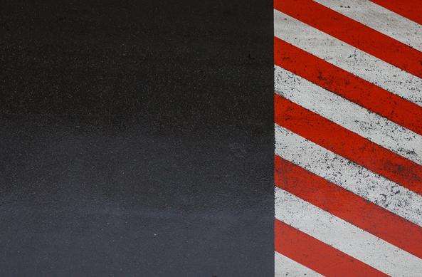 Minimalistic overhead view of a portion of dark blue asphalt and red and white stripes of road markings.
