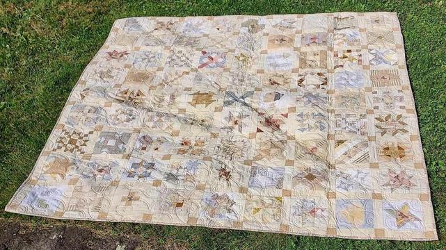 a quilt, it is brown and grey and tan geometric designs, swirly pattern stitching over it 