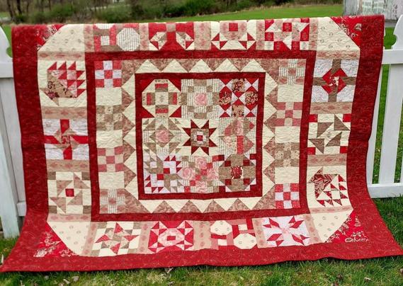 a quilt, it has a thick red border, inside are two thinner interior borders, lots of reds and pins and whites and tans and browns 