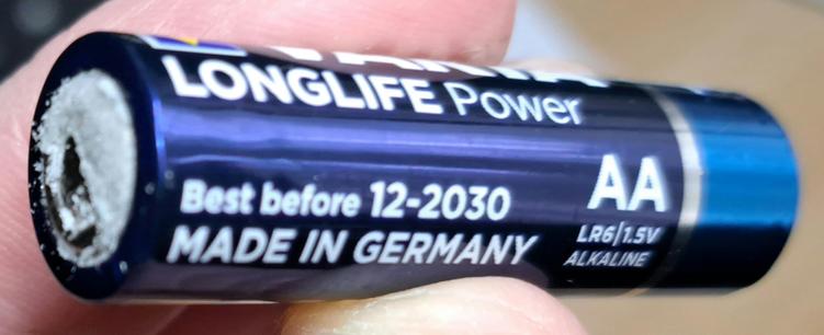 Eine Varta Longlife Power AA Zelle, die angeblich in Deutschland gefertigt wurde und bis Dezember 2030 haltbar sein sollte, aber schon ausgelaufen ist und das Gerät in dem sie war durch Korrosion (am Kontakt erkennbar) geschädigt hat.