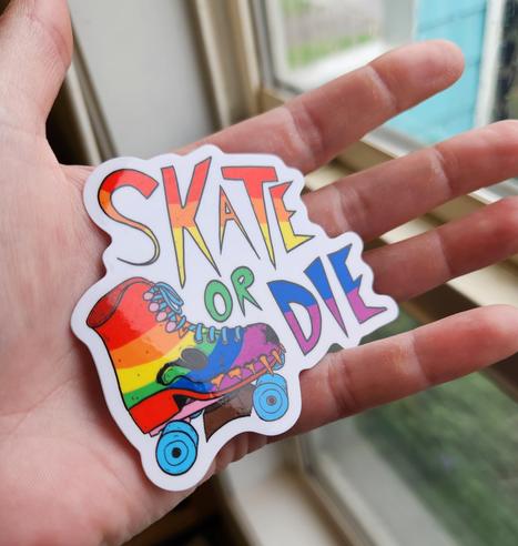 A sticker of a roller skate in the progress pride flag colors. The skate has teeth and is reminiscent of an animal skull and the sticker also says Skate or Die.