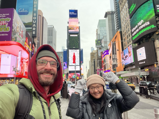 A man and a women in winter clothes pose for a photo in front of the billboards of Times Square 