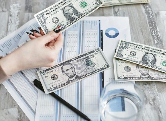 A close-up of a woman's hand handling money on a desk, with a pen and calculator nearby