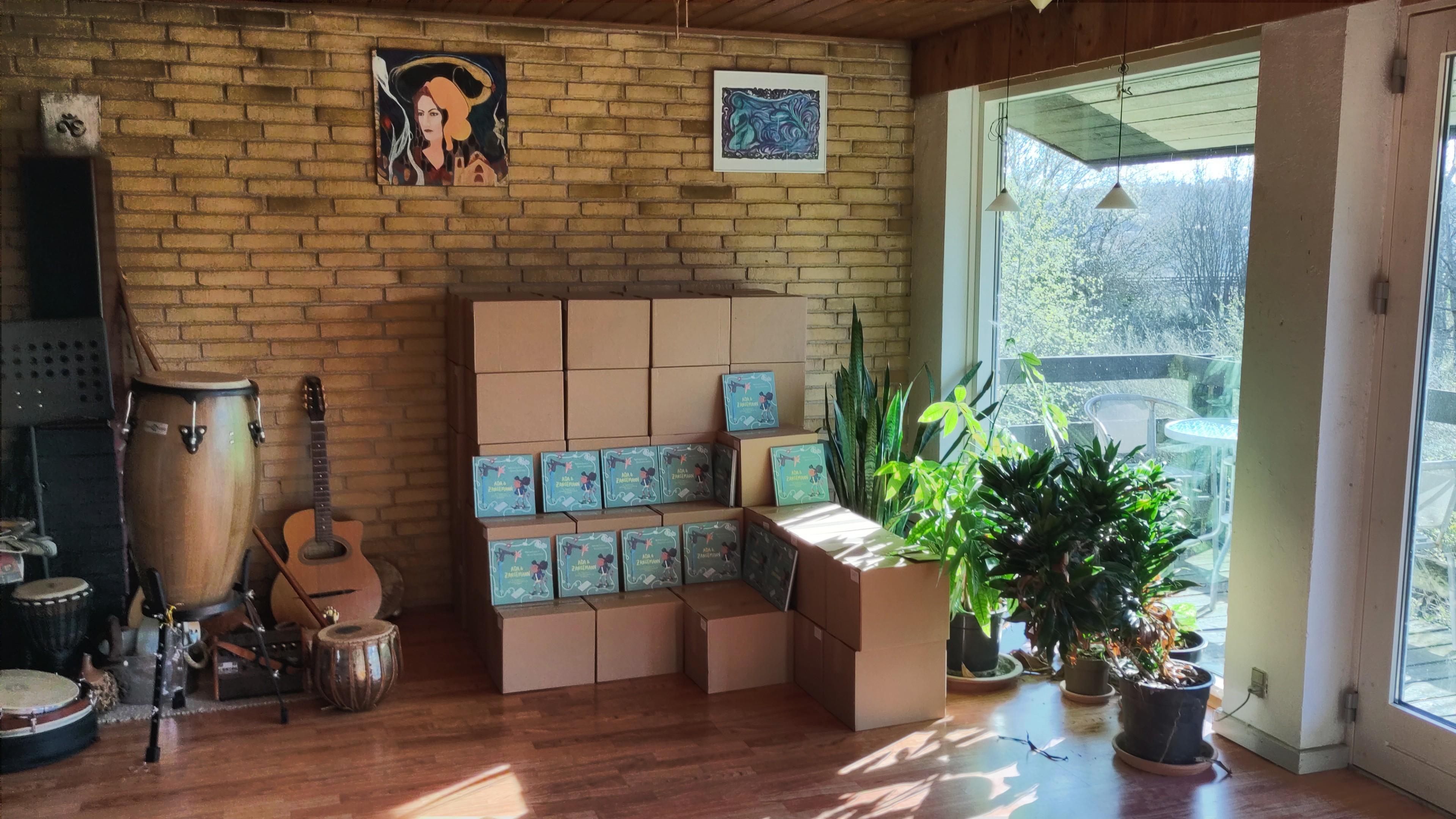 A lot of boxes with books in a living room with some plants, and some music instruments. 