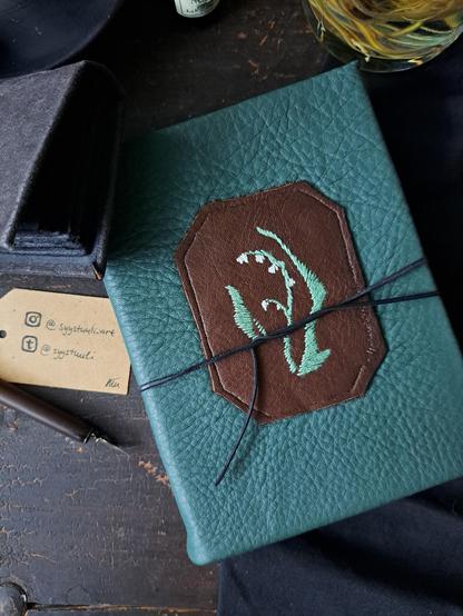 A close up of the cover and the embroidery on it. The boon is being held shut with a black leather string.