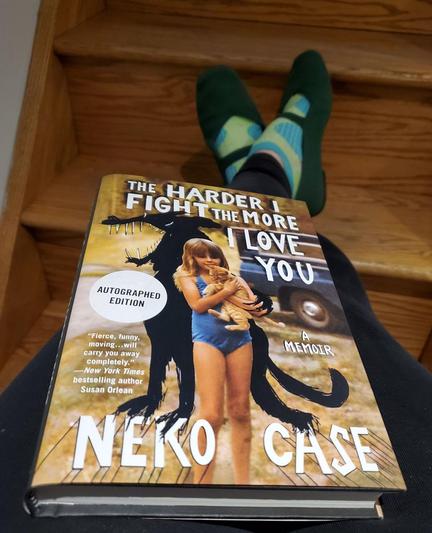 My feet in green mary janes and bright socks are visible on wooden stairs as I hold the book The Harder I Fight the More I Love You by Neko Case (Grand Central Publishing) in my lap.