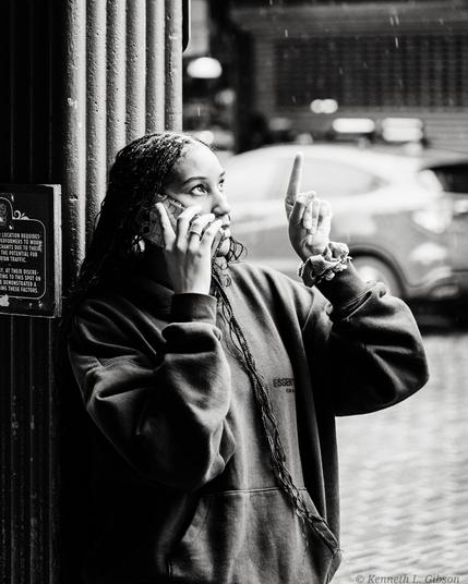 Black and white photo of a woman talking on the phone while pointing upward.