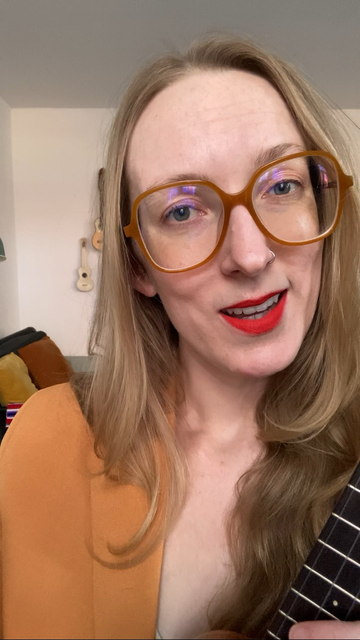 Sage, a whee lady with big glasses, smiles and sings with her ukulele