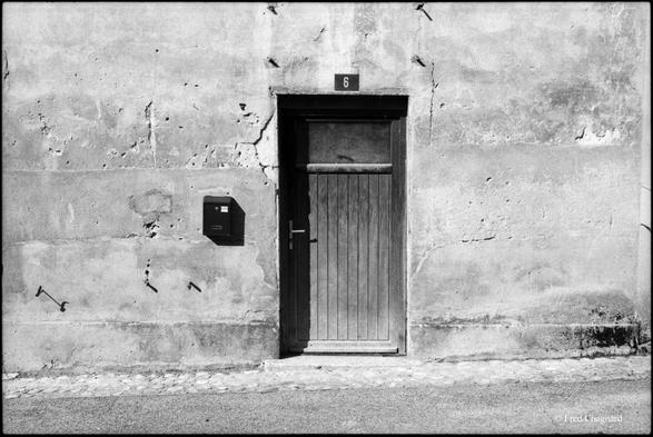 A worn entrance door with a mail box on an old wall without windows. Photo taken with a 35mm camera on black and white negative film.