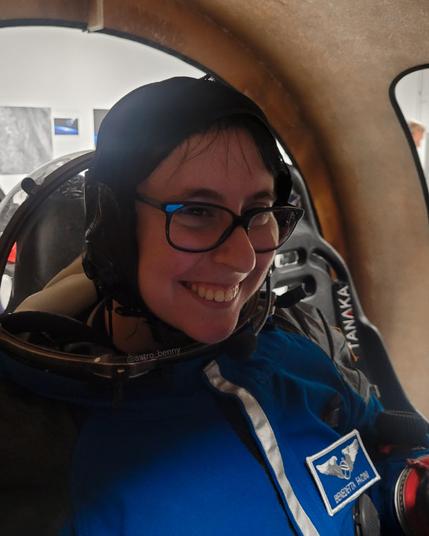 Me wearing a blue spacesuit and smiling inside a spacecraft simulator