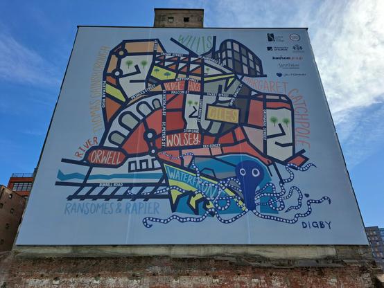 A brand-new locally-themed mural on the side of a tall, ruined silo building by the waterfront