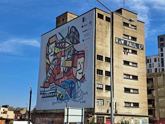 A brand-new locally-themed mural on the side of a tall, ruined silo building by the waterfront