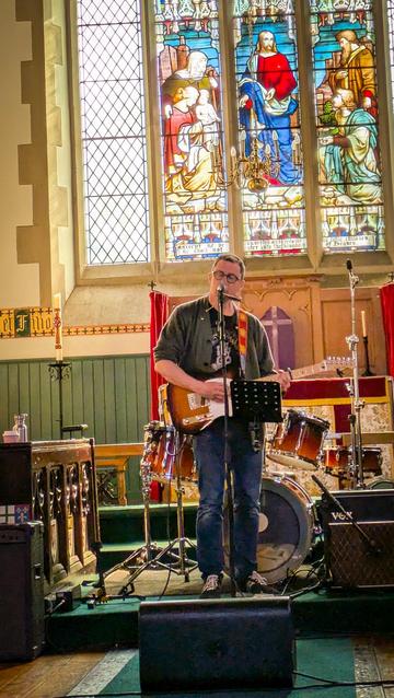 A man on stage with a guitar, behind is a stained glass window