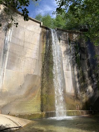 A concrete arch dam has a waterfall cascading over it into a pool