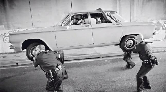 Quatre policiers blancs portent sur l'épaule une voiture à l'intérieur de laquelle se trouvent Kendrick Lamar et ses amis. [image tiré du clip officiel du morceau Alright de Kendrick Lamar]