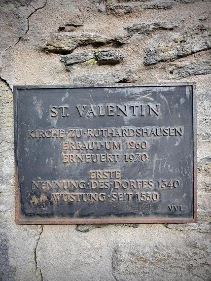 Nahaufnahme der Gedenktafel an der Innenwand der Kirchenruine St. Valentin. Die Inschrift nennt die Bauzeit um 1260, eine Erneuerung 1970 sowie die erste Nennung des Dorfes Ruthardshausen im Jahr 1340. Das Dorf wurde um 1550 zur Wüstung