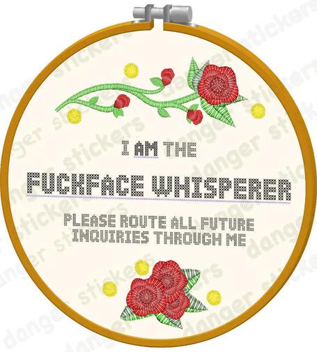 a sticker design of an embroidery hoop that says "I AM the FUCKFACE WHISPERER. Please route all future inquiries through me". There's pretty flowers on it, too.