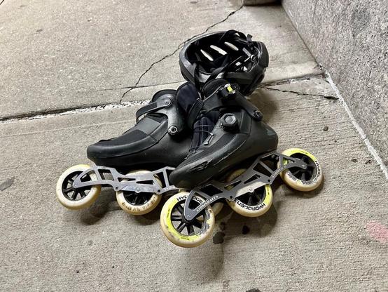 Photo of a pair of inline skates and a helmet lying on the sidewalk. The skates are Rollerblade Revv boots mount on Striker II 3x110 frames with Rollerblade Hydrogen wheels. Who cares about the helmet.