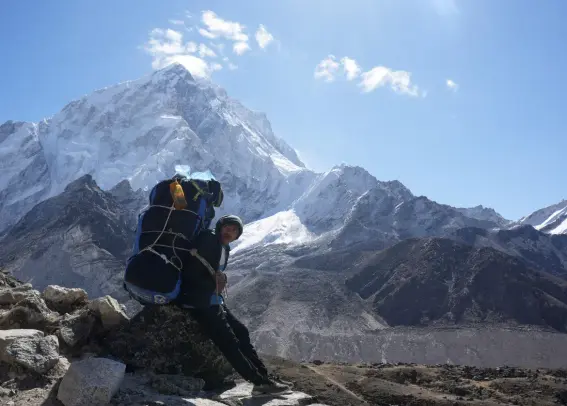 A porter takes a break while on his way to Everest base camp at Lobuche with Mt Everest in the background on a clear day.