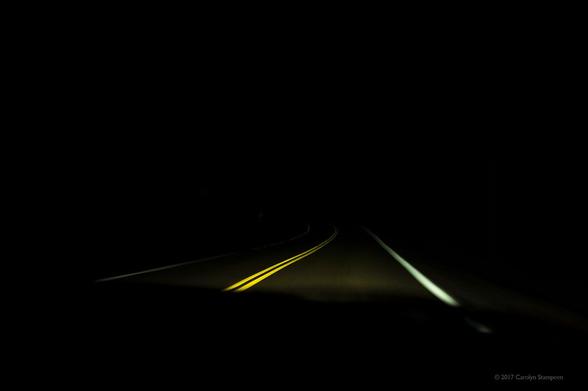 Image is black except yellow and white reflective paint on the road, which occupies about 1/4 of the image, above the hood of the car. 