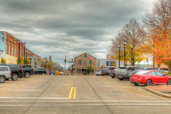 A quiet street scene unfolds in a small town with parked cars lining both sides of the road and a single building in the distance.