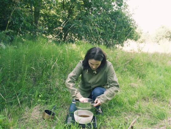 Brown-haired woman in woodland clearing making eco-friendly laundry soap from foraged ivy leaves (Hedera helix)