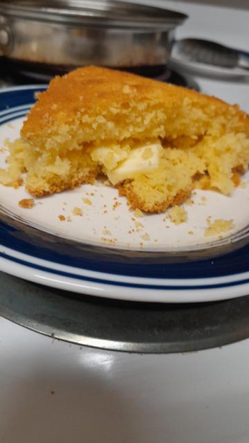 A slice of cornbread on a white plate with a blue circle around the outside and a little bit of butter hanging out the cornbread