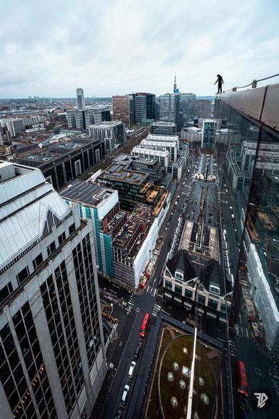 silhouette of a girl standing on the edge of a tall building with the city below and reflects in the glass windows